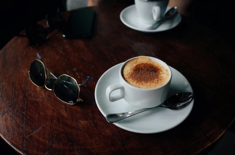 a cup of cappuccino and two spoons sit on a wooden table