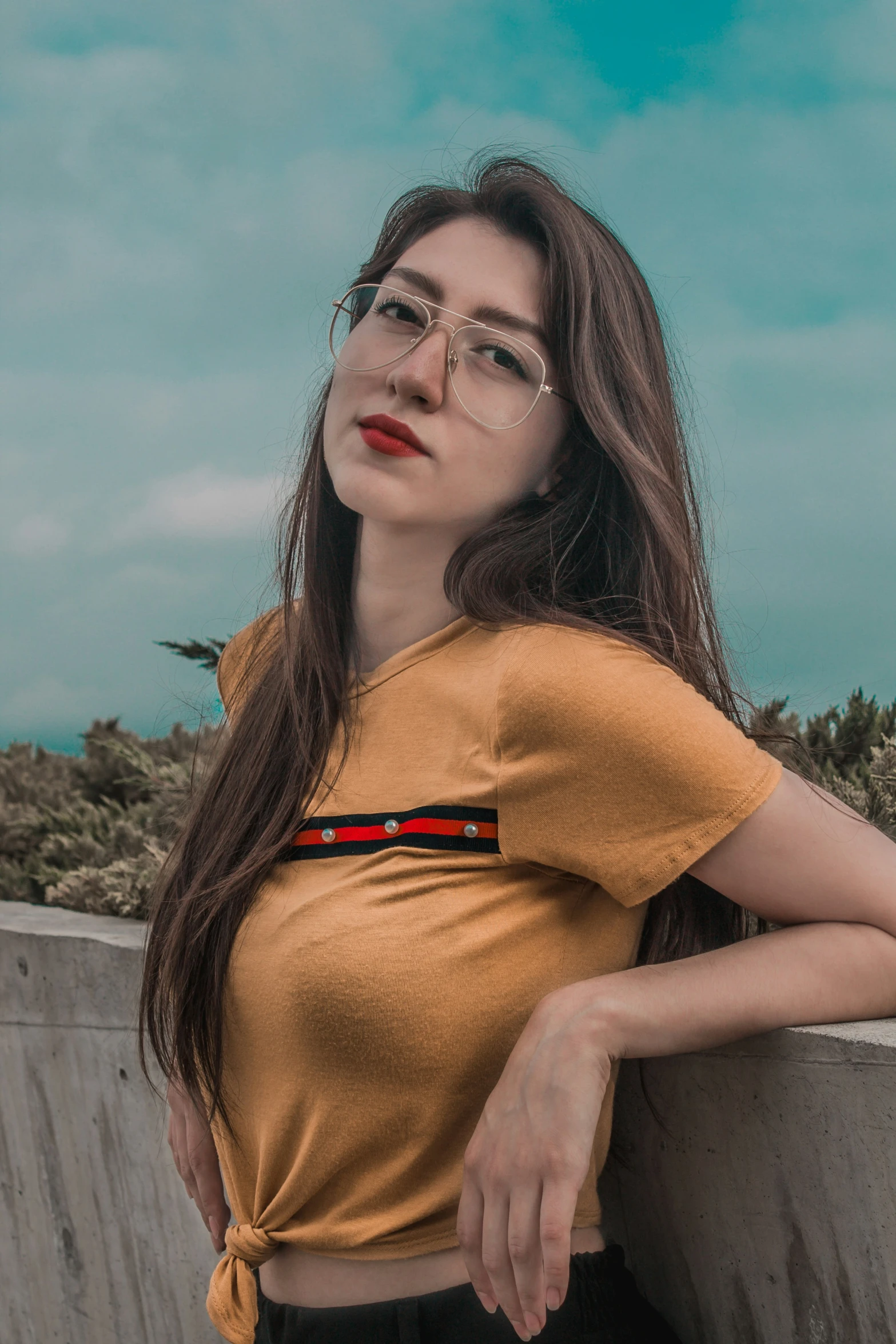 a woman wearing glasses leaning against a cement wall