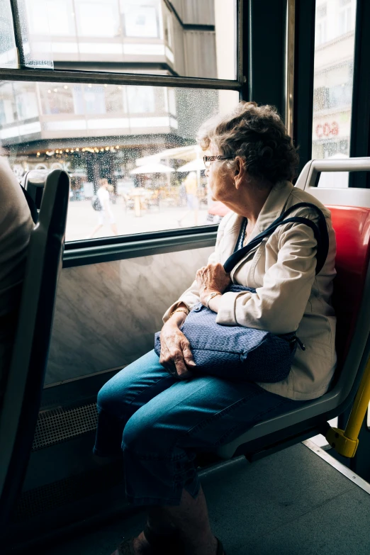 an older woman in glasses sits at a window on a train