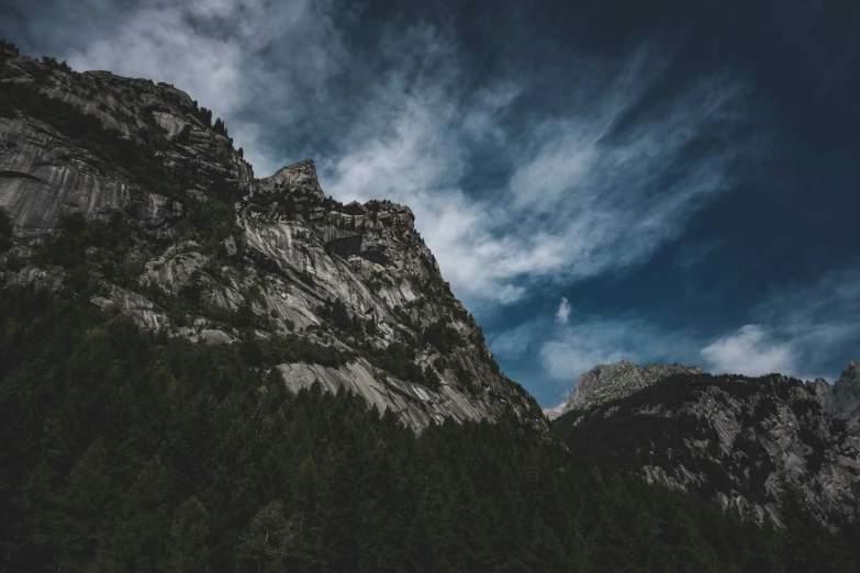 a large mountain covered in trees under a cloudy blue sky