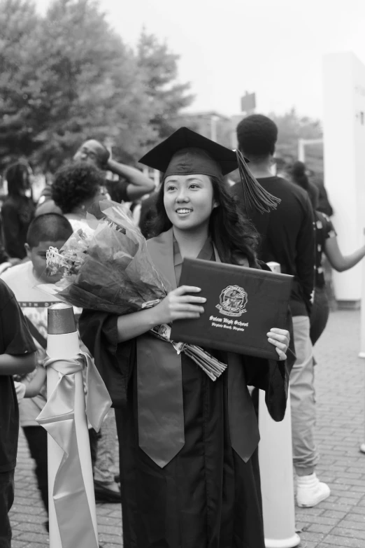  at graduation holding flowers and a plaque