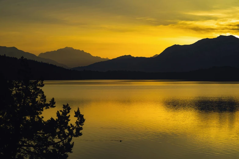 the sun sets in a lake with trees in the foreground