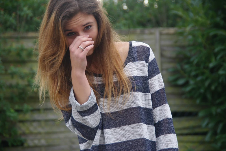 a girl is covering her nose and standing in the grass