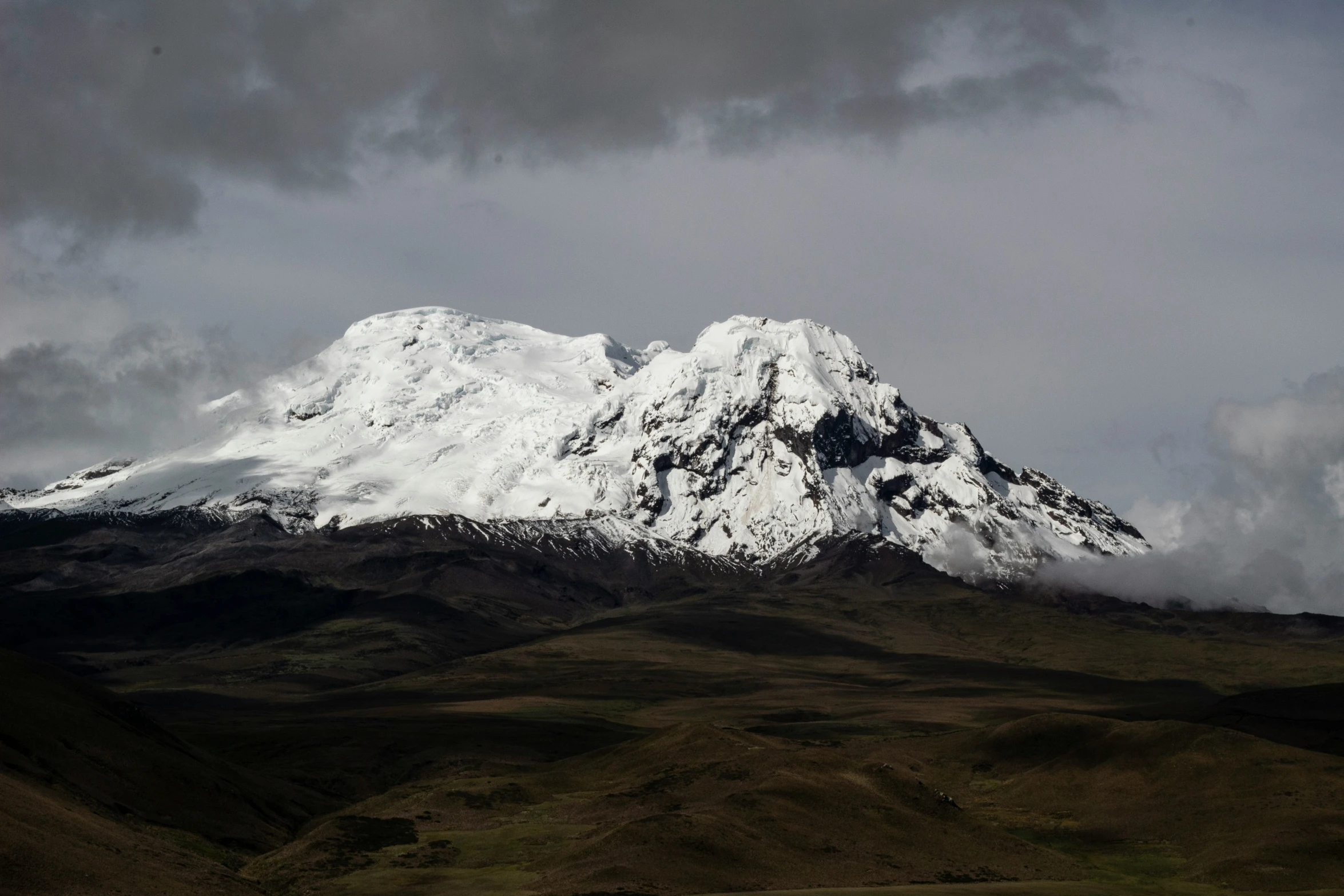 a snow capped mountain standing over the green hills