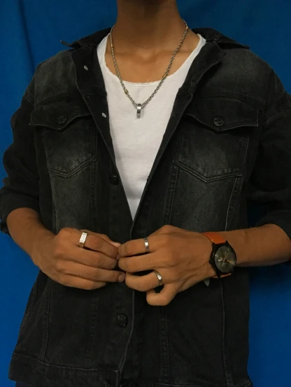 a young man wearing a black denim jacket holds out his wrist ring