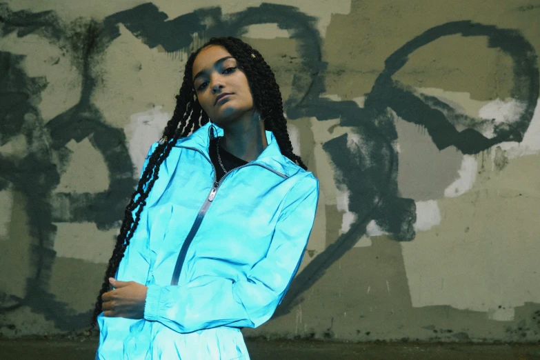 a man in a blue coat with dreadlocks standing near graffiti