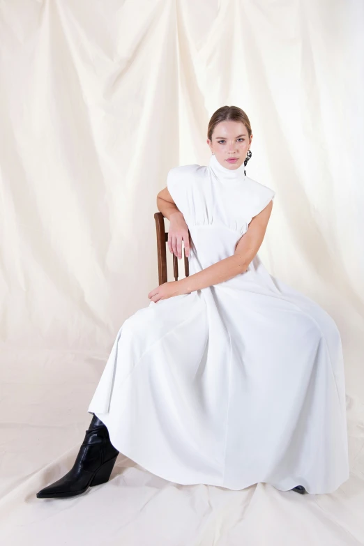 a woman wearing a white dress sitting down on a wooden chair