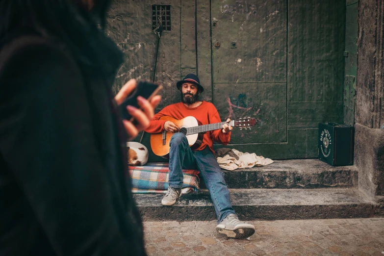 a man sitting outside playing guitar, phone and singing