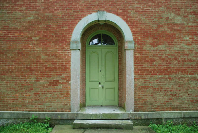 an arched doorway to a brick building, with green door
