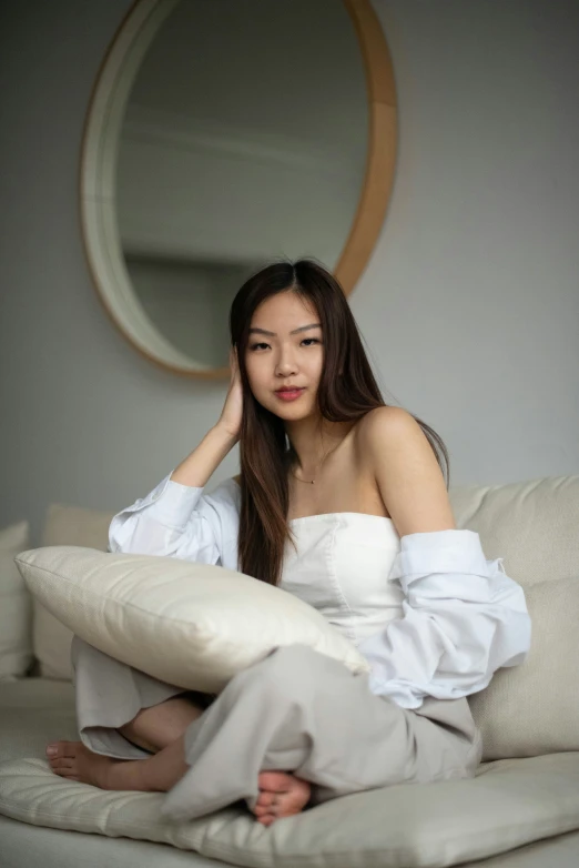 a woman sits on a bed and covers her face with her pillow