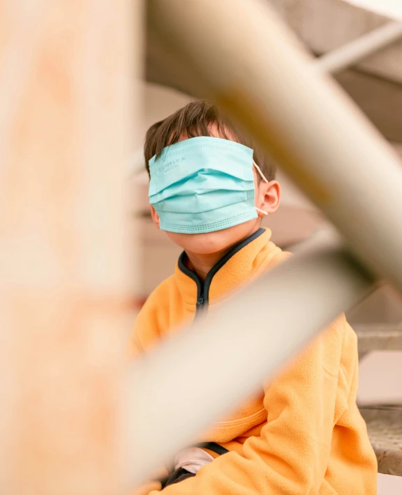 a boy wearing a face mask and sitting on the ground