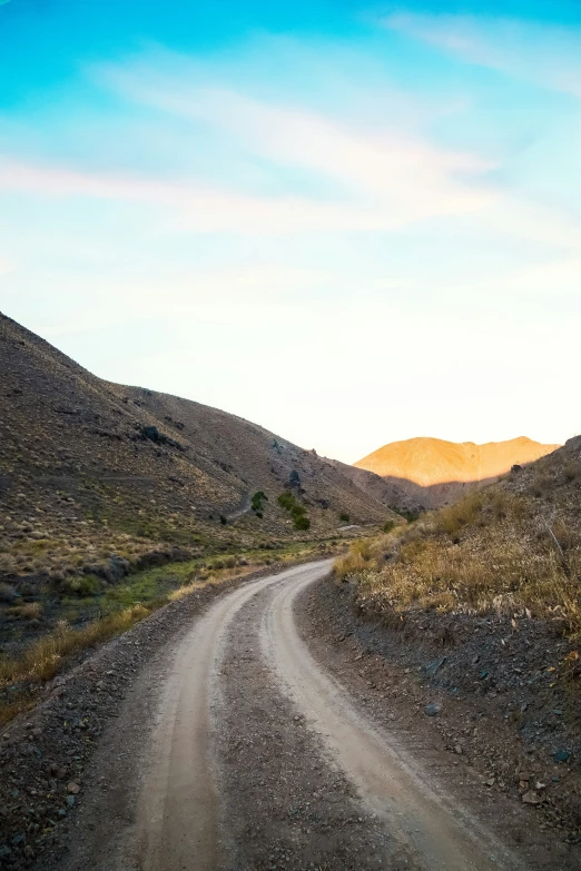 a paved dirt road passing between hills