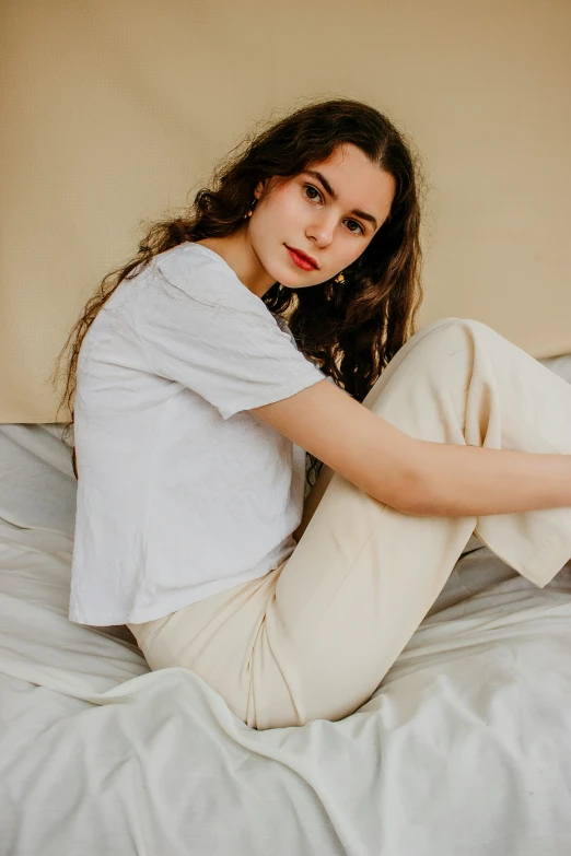 a woman sitting on top of a bed wearing beige pants