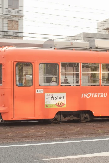 an orange tram with japanese writing and people in the window