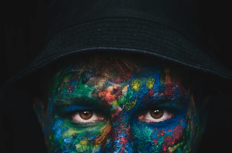 a man with multicolored face paint in the dark