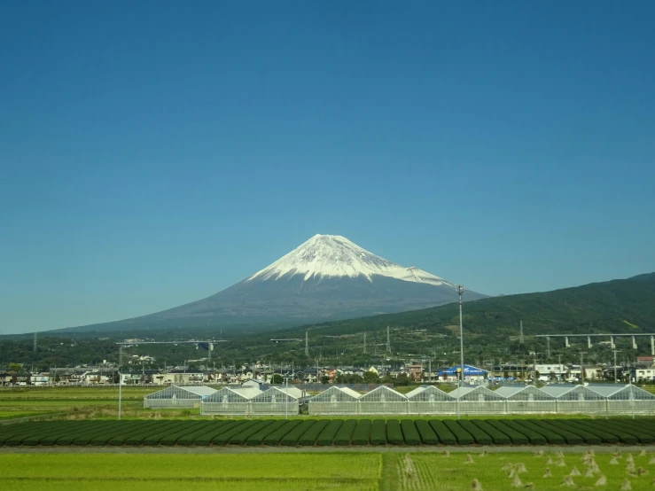 snow - capped mountain towering over farmland in front of a city