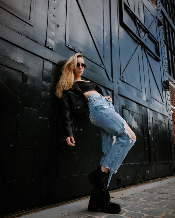 an attractive woman leans against a black metal wall