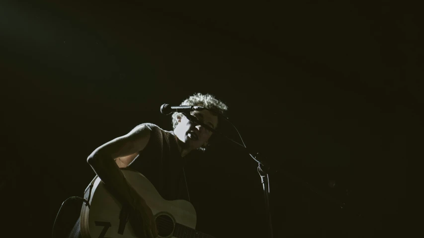 a man holding a guitar sings into a microphone