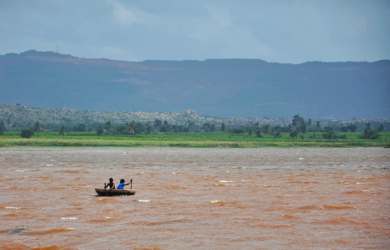 three people are on a small boat in a brown river