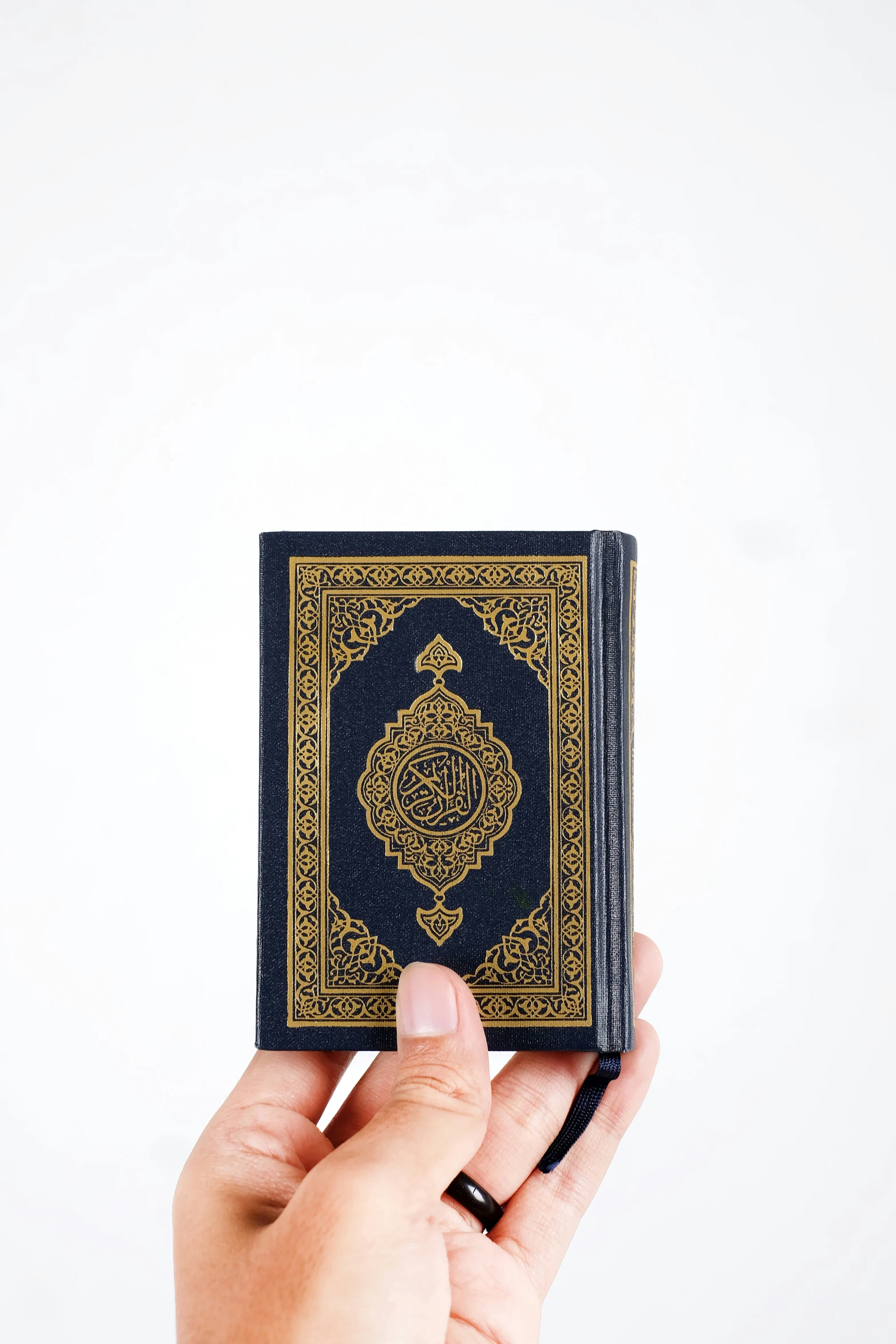 a hand holds a black and yellow islamic prayer book