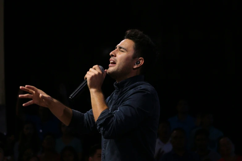 an asian male standing in front of an audience holding a microphone up to his mouth