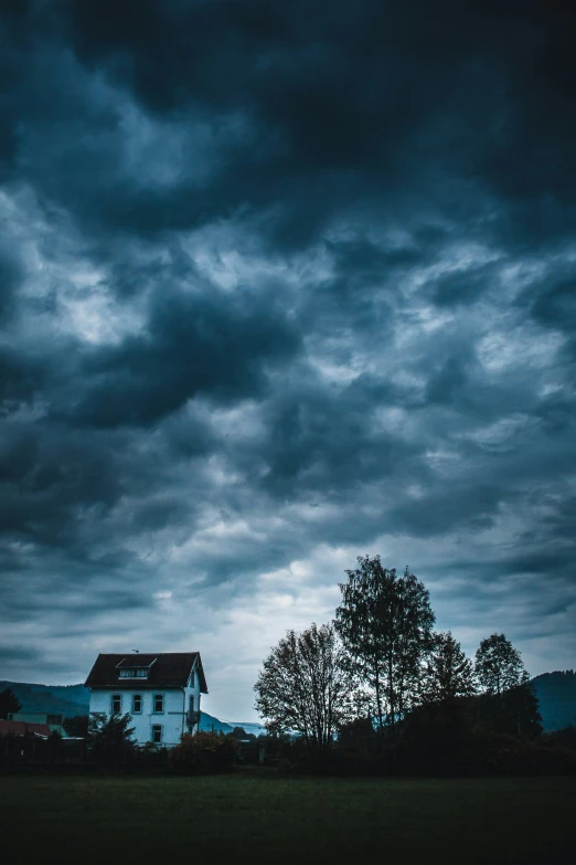 a house on top of a hill with a storm coming over the house