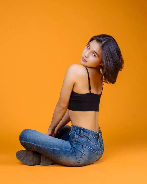 a young woman posing in jeans against an orange background