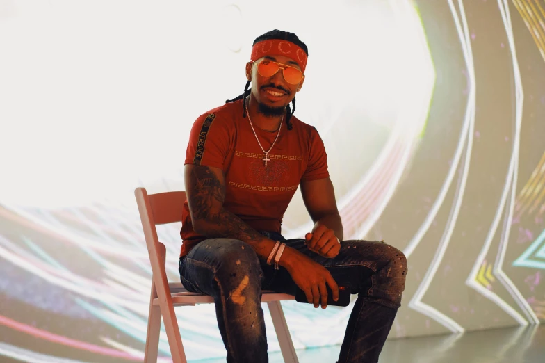 a black man with tattoos and red shirt sitting on a white chair