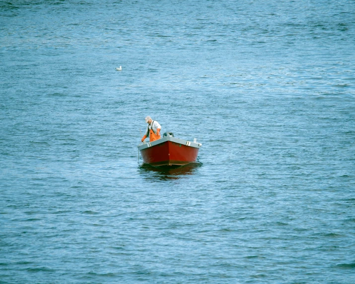 a man is out on the water in a small red boat