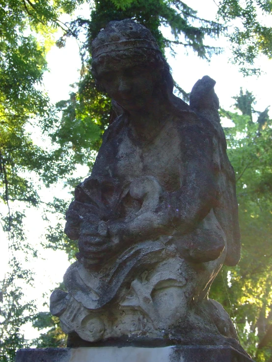 an old statue sitting in the shade by a tree