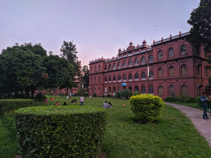 an ornately designed red brick building with hedges and a lot of people