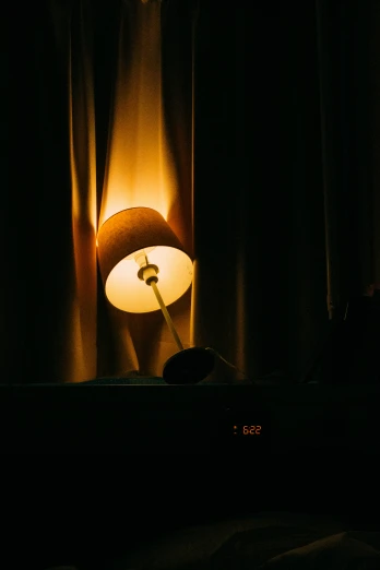 the lamp in the dark shines as a shadow is cast on the curtained surface