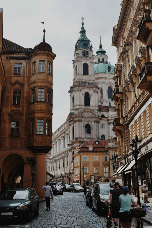 the people are standing near the buildings on the cobblestone street