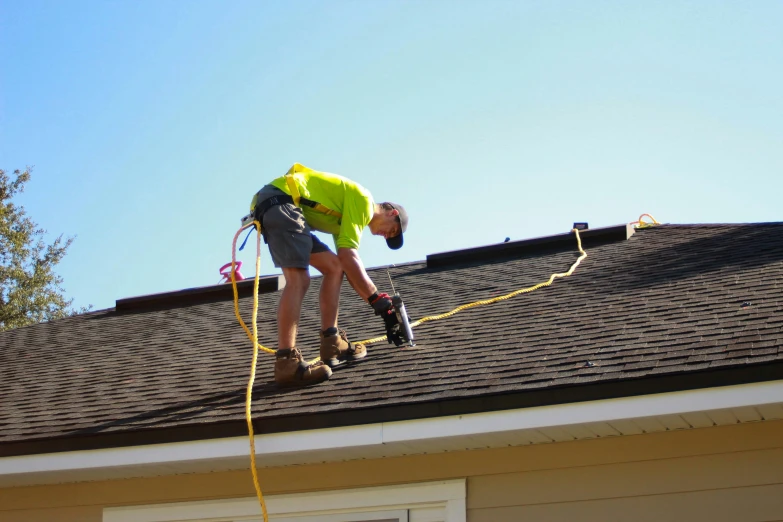 a man working on an asphalt roof with a nail gun