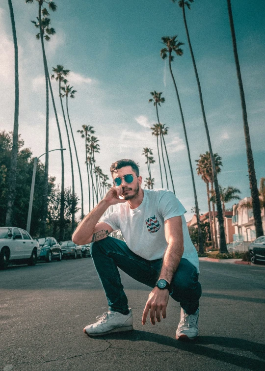 a man standing next to some palm trees while holding his hand on his hip