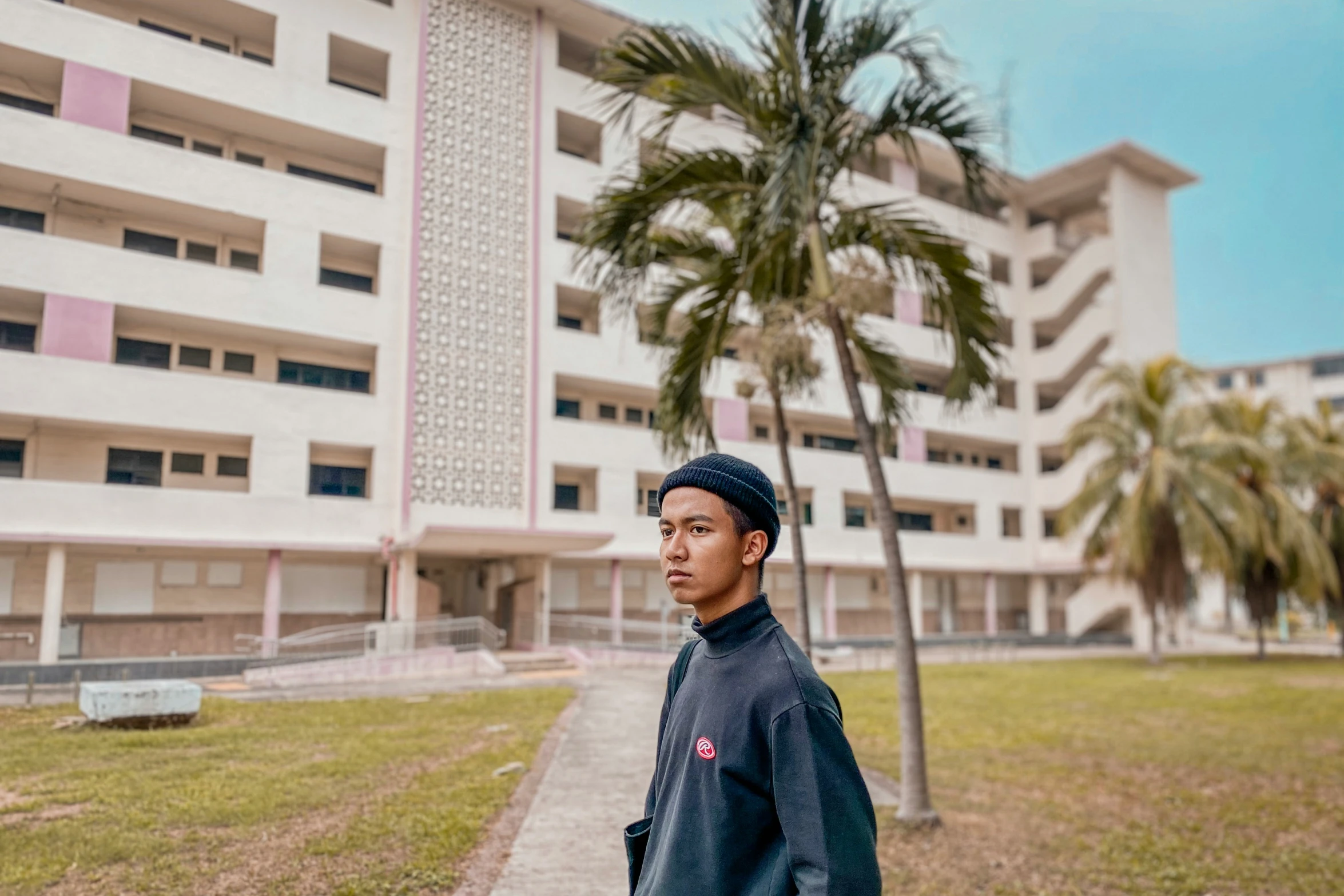 a young man in a blue hoodie standing in front of a large white building