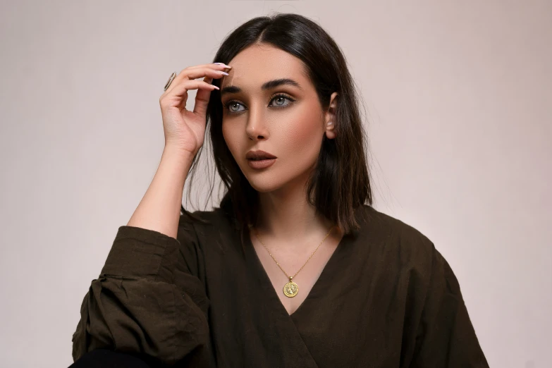 a woman wearing a brown shirt holds her hand to her face