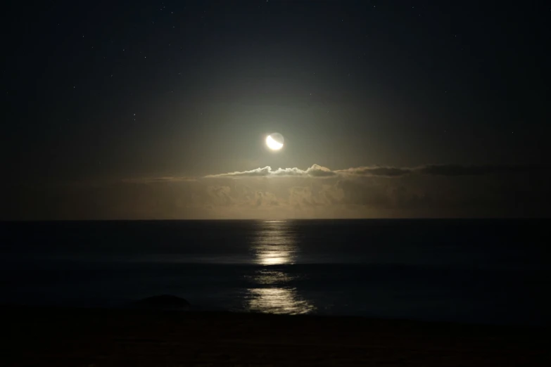 a view of the ocean from the shore, moon over water