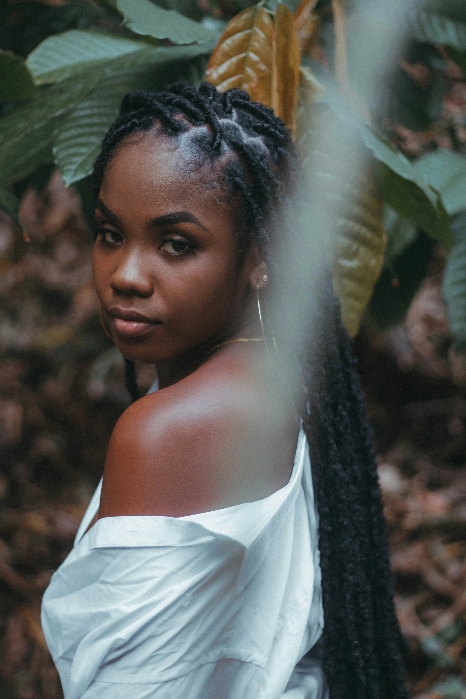 a woman with cornrows wearing white is standing near a tree