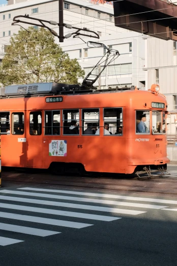 an orange tram going down the street in front of some buildings