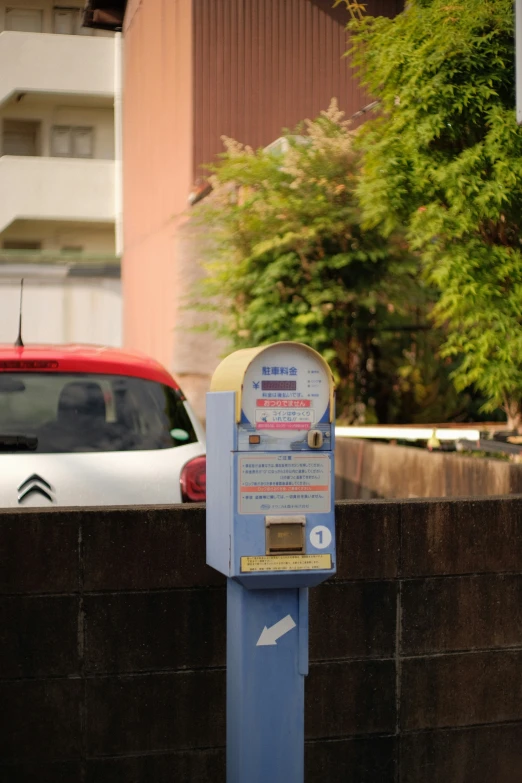 a parking meter sitting next to a wall in front of a red car