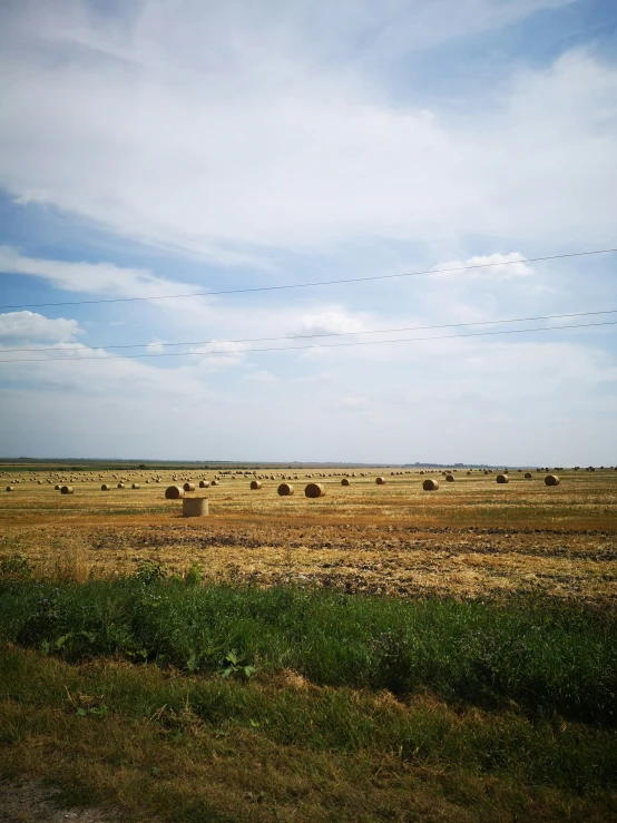 a farm field has bales in the foreground and a plane flying overhead