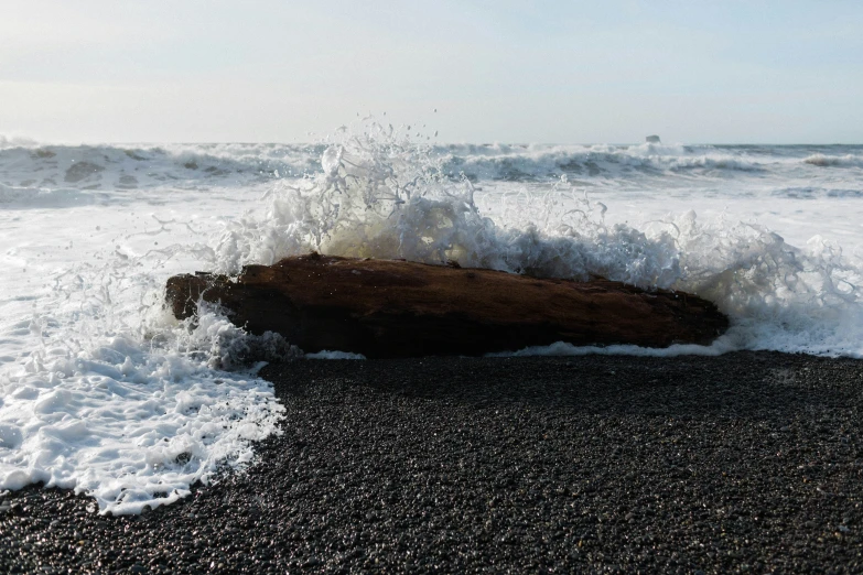 crashing surf next to large rock on sandy beach