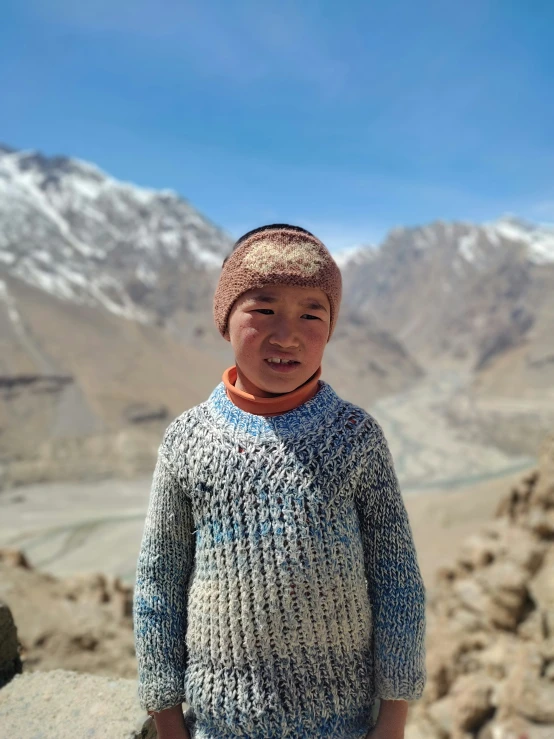 a smiling little boy stands in front of snowy mountains