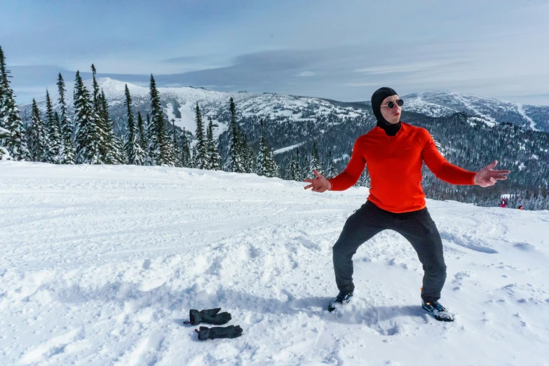 man standing in the snow with his arms out and a pair of skis sitting on the snow