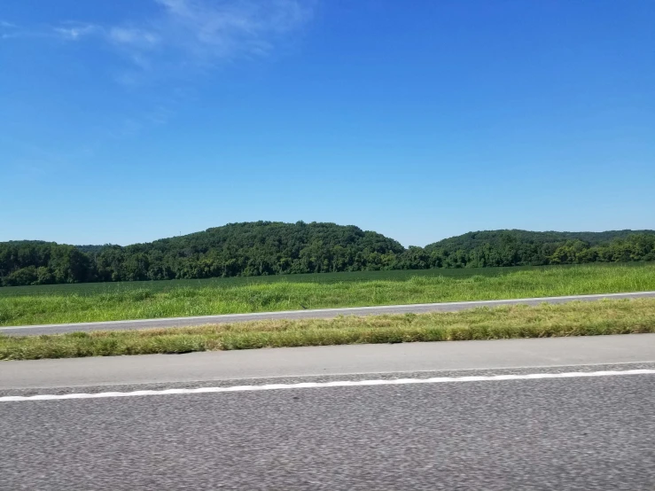 a view from the side of a road that shows several green hills