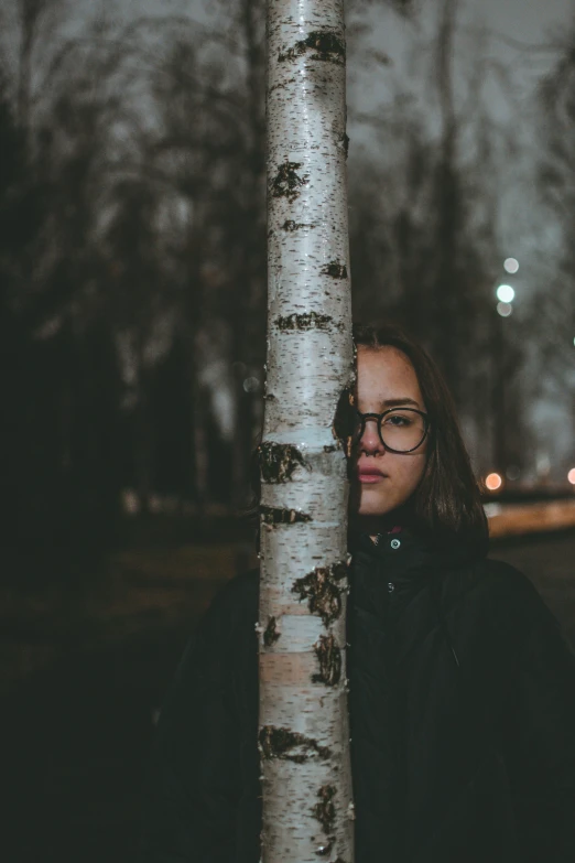 a woman wearing glasses leans against a tree