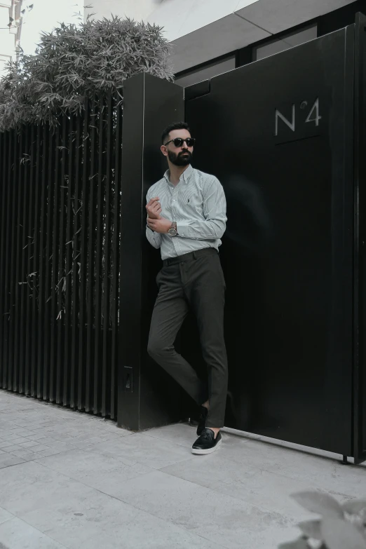 the man is posing against the wall wearing sunglasses