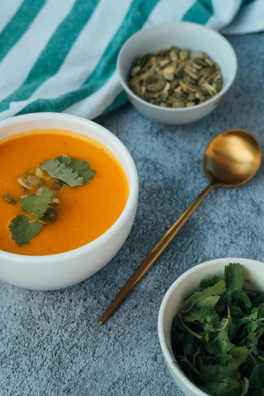 a bowl with carrot soup and two bowls of food on a towel