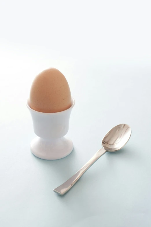 spoon next to an egg and an empty plate on a table